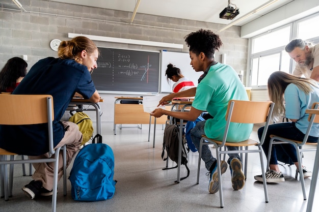 Zwei männliche Gymnasiasten arbeiten zusammen und der Lehrer hilft dem Schüler bei den Hausaufgaben