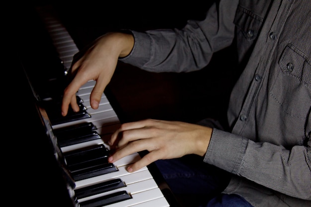 Zwei männliche Hände auf dem Klavier. Handflächen liegen auf den Tasten und spielen das Tasteninstrument in der Musikschule. Schüler lernt zu spielen. Hände Pianist. schwarzer dunkler Hintergrund.