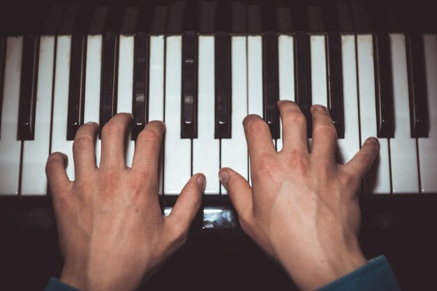 Foto zwei männliche hände auf dem klavier palmen liegen auf den tasten und spielen das tastaturinstrument in der musikschule schüler lernt zu spielen hände pianist schwarzer dunkler hintergrund top-ansicht