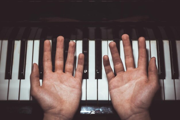 Foto zwei männliche hände auf dem klavier palmen liegen auf den tasten und spielen das tastaturinstrument in der musikschule schüler lernt zu spielen hände pianist schwarzer dunkler hintergrund top-ansicht