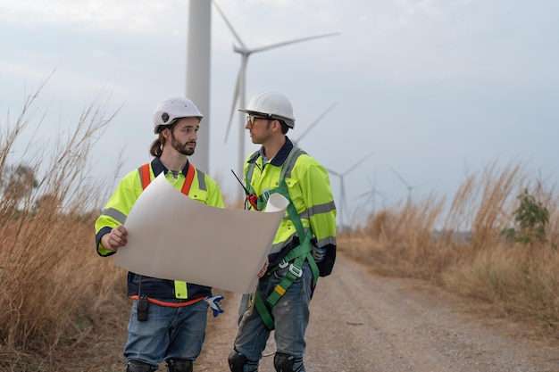 Zwei männliche Ingenieure diskutieren über die Wartung einer Windkraftanlage in einem Windpark für elektrische Energie