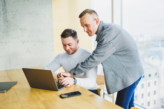 Zwei männliche Kollegen bei der Arbeit mit einem Laptop im Büro Zwei zielorientierte Unternehmer arbeiten an einem modernen Arbeitsplatz zusammen Zwei junge Geschäftsleute arbeiten in einem hellen Büro