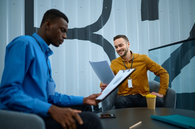 Zwei männliche Mitarbeiter, Konferenz im IT-Büro. Professionelle Teamarbeit und Planung, Gruppen-Brainstorming, modernes Firmeninterieur im Hintergrund