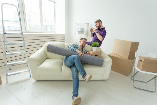 Zwei männliche Studentenfreunde halten ihre Sachen in den Händen und sitzen im Wohnzimmer einer neuen Wohnung. Einweihungskonzept.