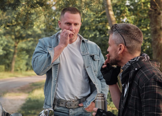 Zwei Mannfreunde von Motorradfahrern auf Motorrädern, die am Straßenrand rauchen und sich unterhalten