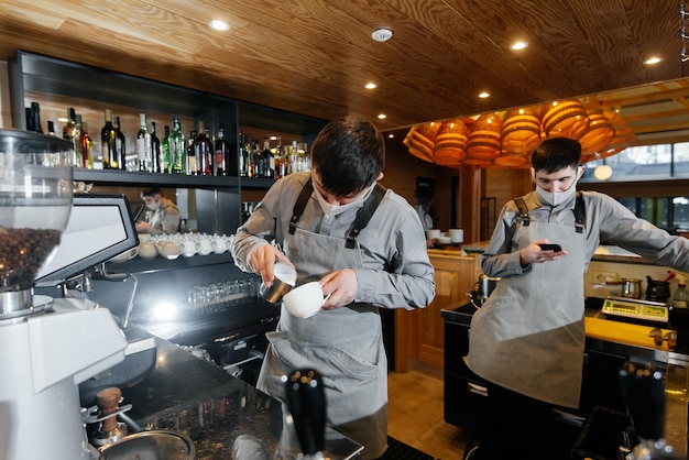 Zwei maskierte Baristas bereiten an der Bar im Café exquisiten köstlichen Kaffee zu Die Arbeit von Restaurants und Cafés während der Pandemie