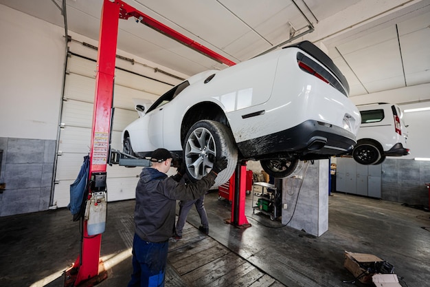 Zwei Mechaniker in Service-Reparaturstation arbeiten mit Muscle-Car im Aufzug