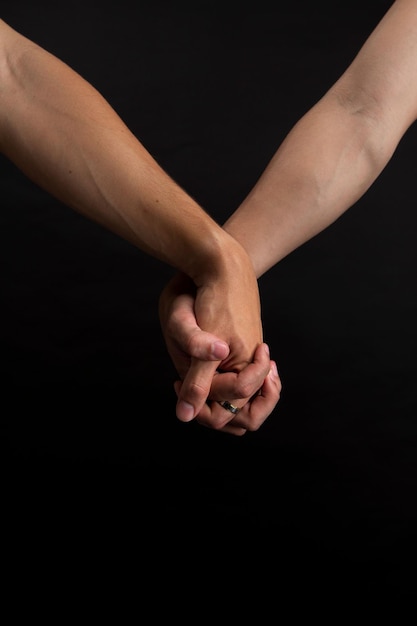 Zwei Menschen halten sich gegenseitig die Hände auf dem schwarzen Hintergrund, vertikal, Nahaufnahme