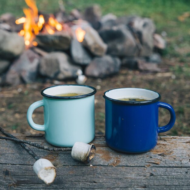 Zwei Metallbecher mit Tee und Marshmallows feuern im Hintergrund