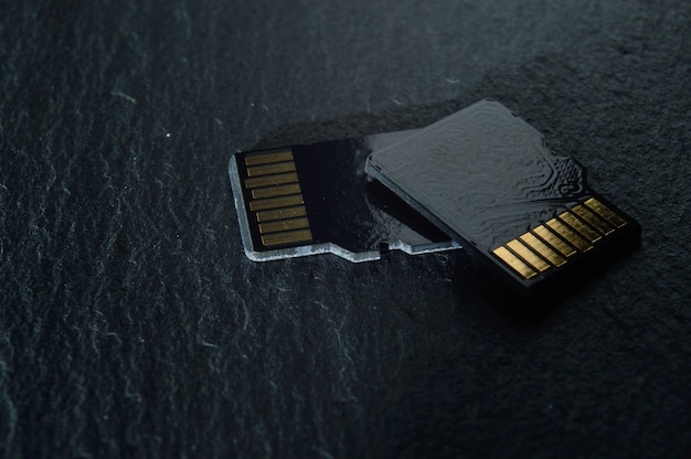 Zwei Micro-SD-Karten liegen auf einem dunklen strukturierten Hintergrund übereinander, mit goldenen Kontakten oben. Nahaufnahme.