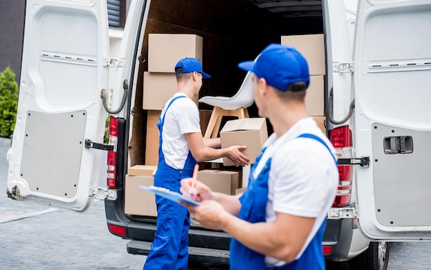 Zwei Mitarbeiter des Umzugsunternehmens entladen Kisten aus dem Minibus in das Haus des Kunden