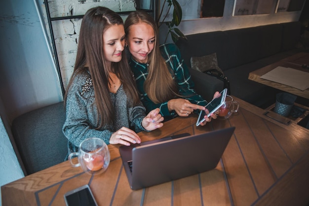 Zwei moderne Frauen, die sich im Café treffen. Arbeiten am Laptop- und Tablet-Konzept