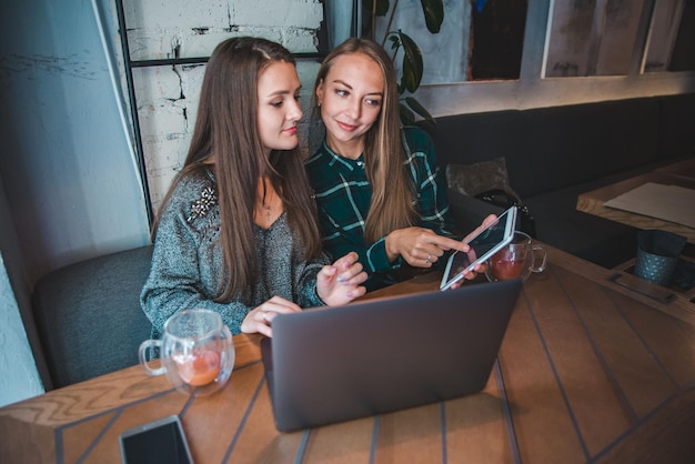 Zwei moderne Frauen, die sich im Café treffen und an einem Laptop-Ameisentablett arbeiten