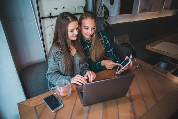 Zwei moderne Frauen, die sich im Café treffen und an einem Laptop-Ameisentablett arbeiten