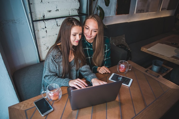 Zwei moderne Frauen, die sich im Café treffen und an einem Laptop-Ameisentablett arbeiten