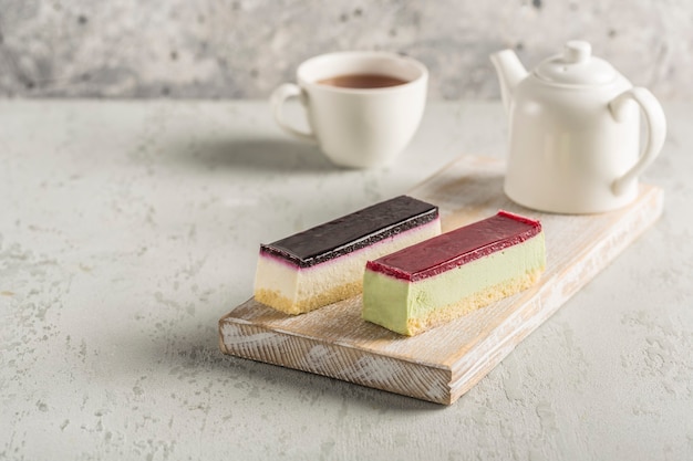 Zwei Moussekuchen mit unterschiedlichem Zuckerguss auf einem Holzbrett mit einer Teekanne und einer Tasse Tee