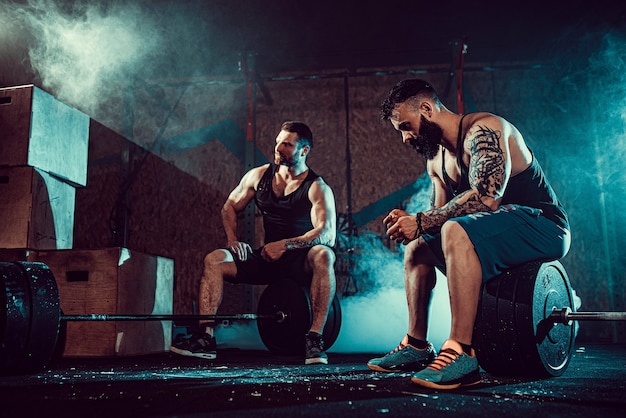 Zwei muskulöse bärtige tätowierte Athleten entspannen sich nach dem Training und heben schweres Gewicht