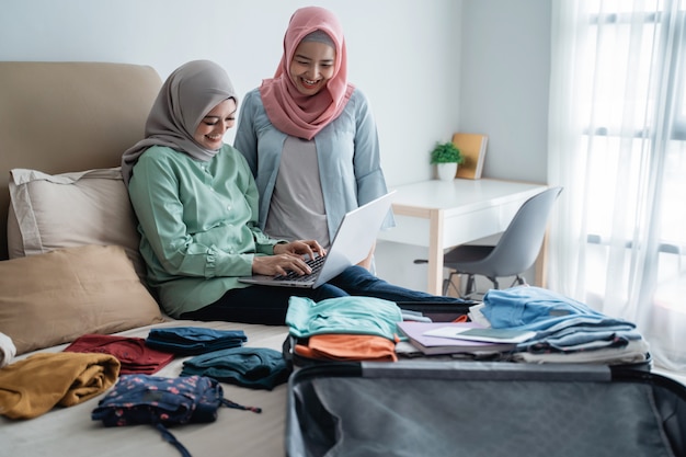 Zwei muslimische Frauen, die Laptop mit vollem Koffer benutzen