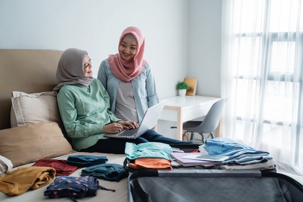 Zwei muslimische Frauen, die Laptop mit vollem Koffer benutzen