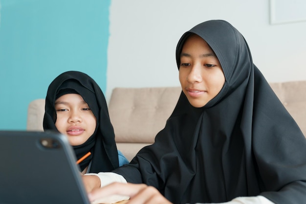 Foto zwei muslimische mädchen lernen online über das internet auf dem tablet im wohnzimmer zu hause asiatische grundschulkinder beobachten computertabletten konzept der bildung zu hause