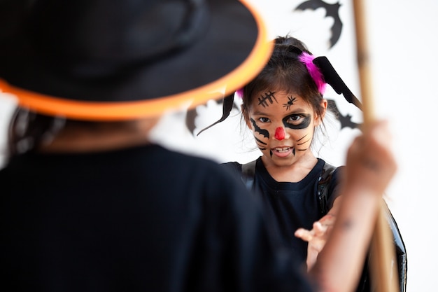 Zwei nette asiatische Kindermädchen, die Halloween-Kostüme und Make-up haben Spaß auf Halloween-Feier tragen