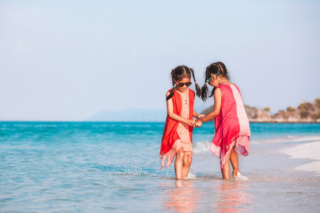 Zwei nette asiatische Kindermädchen, die Hand halten und zusammen auf Strand spielen