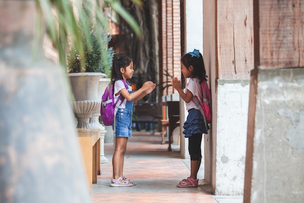 Zwei nette asiatische Kindermädchen mit der Schultasche, die zusammen nach der Schule in der Schule spielt
