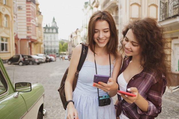 Zwei nette Frauen, die, eine Karte am intelligenten Telefon überprüfend lächeln und zusammen reisen