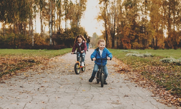 Zwei nette Kinder, die mit dem Fahrrad fahren, spielen fröhlich in einem Park, während die Sonne untergeht