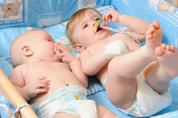 Zwei Neugeborene in Windeln, die in der hölzernen Krippe auf blauer Decke mit Brustwarzen im Mund liegen