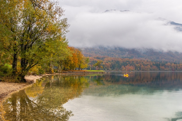 Zwei nicht wiedererkennbare Touristen unternehmen an einem schönen Herbsttag eine Kanutour rund um den malerischen Bohinj-See. Reisende fahren mit dem Kajak zum Ufer und Ferienwohnungen, die sich zwischen Bäumen verstecken, deren Farben sich ändern