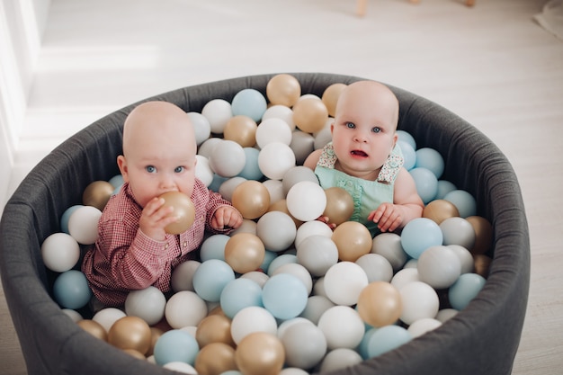 Zwei niedliche kleine Kleinkind posiert sitzend im Eimer mit bunten Bällen, die Spaß haben