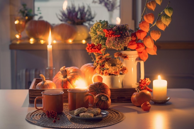 Zwei orangefarbene Tassen Tee und Herbstdekor mit Kürbisblumen und brennenden Kerzen auf dem Tisch