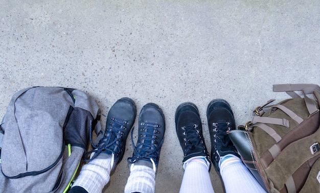 Zwei Paar Beine in Stiefeln zum Wandern stehen auf dem grauen Bürgersteig mit Rucksäcken.