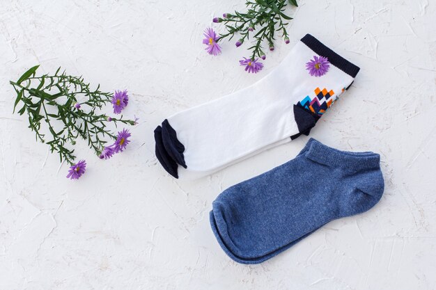 Zwei Paar Damensocken und Blumen auf dem weißen strukturierten Hintergrund, Ansicht von oben.