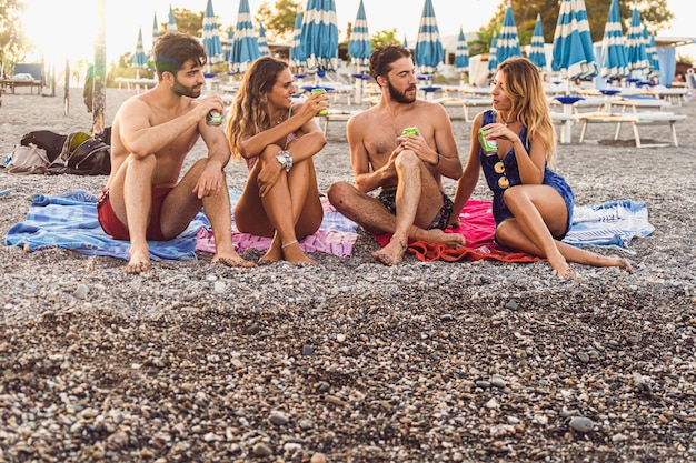 Zwei Paare junger Leute verbringen glücklich Zeit an einem Kiesstrand und unterhalten sich miteinander