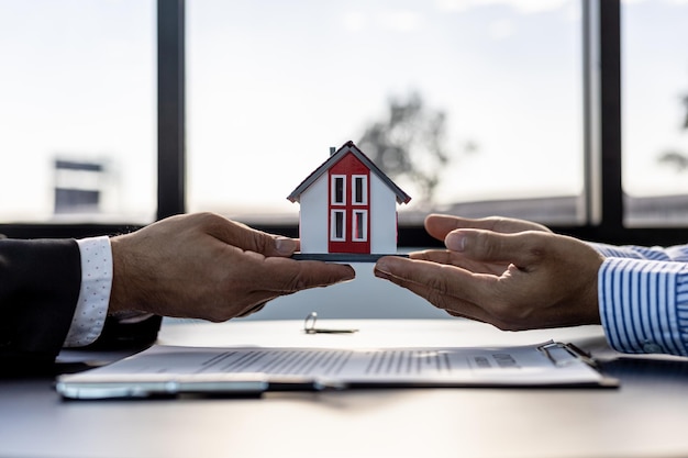 Zwei Personen halten ein kleines Musterhaus, der Hausverkäufer übergibt das Haus nach Vertragsunterzeichnung und Hausbesichtigung an den Kunden. Ideen für den Immobilienhandel.