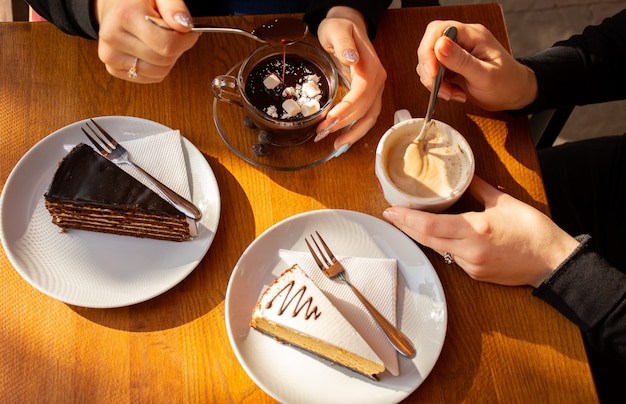 Zwei Personen halten frische Kuchen, Kaffee mit Sahne und heiße Schokolade auf dem Tisch in einem Café