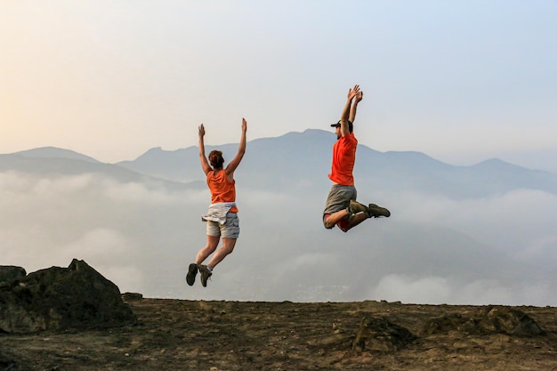 Zwei Personen in orangefarbenen Poloshirts springen auf einen Berg.