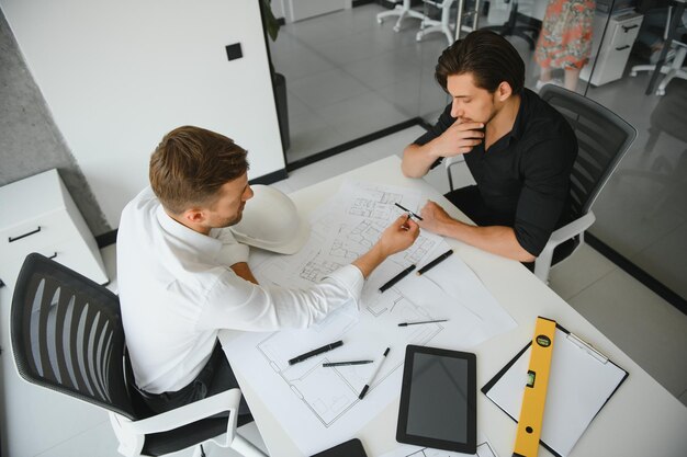 Zwei Personen sitzen vor einem Bauplan und unterhalten sich über die Architektur