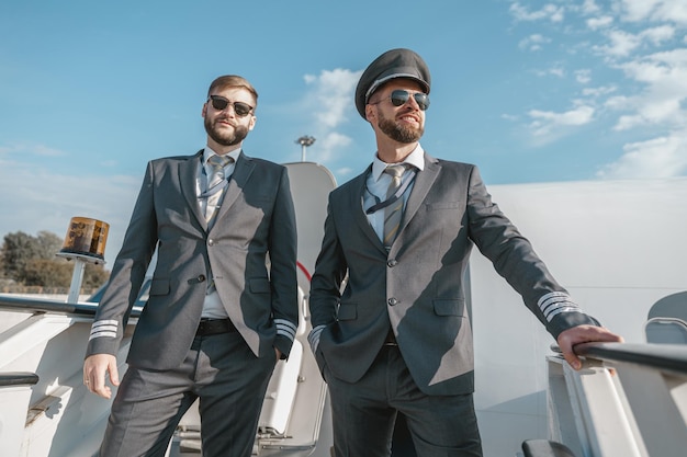 Zwei Piloten mit Sonnenbrille stehen vor dem Flug auf dem Flughafen auf der Flugzeugtreppe