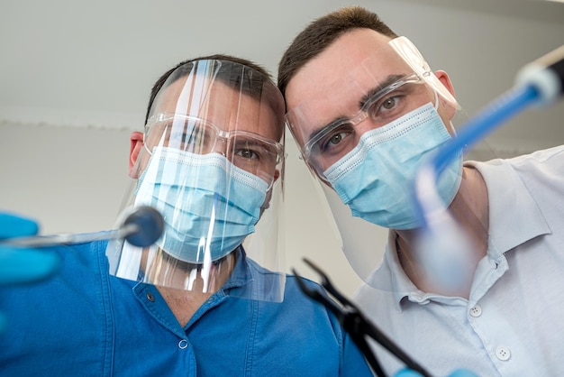 Zwei professionelle selbstbewusste Zahnärzte posieren in der Nähe eines Behandlungsstuhls in einer Klinik