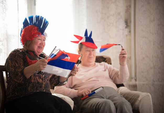 Zwei reife Frauen, die in russischen Accessoires sitzen und russische Flaggen halten