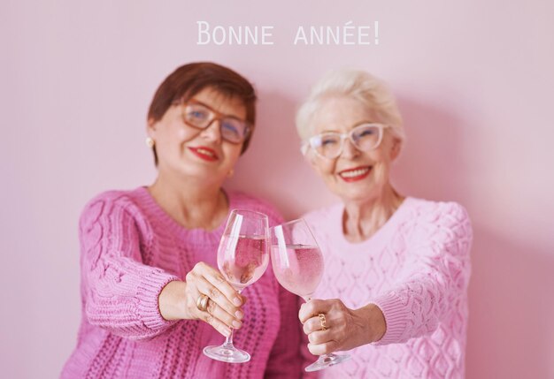 Zwei reife Frauen in rosa Pullover trinken Wein und feiern