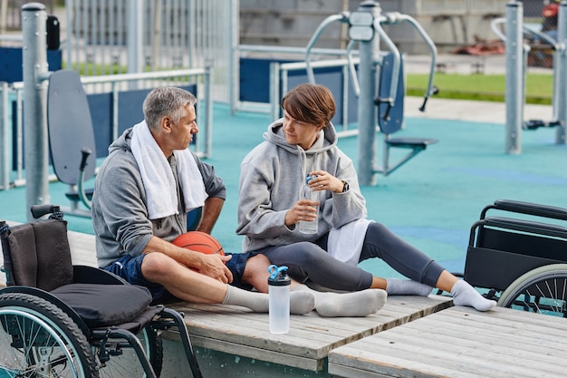 Zwei reife Freunde, die auf der Bank sitzen, Wasser trinken und nach dem Sporttraining miteinander reden...