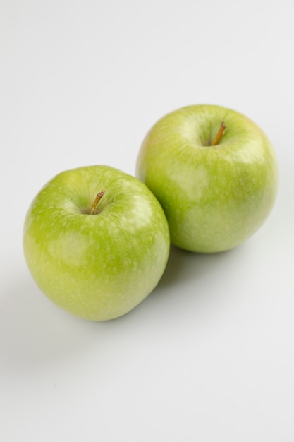 Zwei reife grüne Äpfel auf weißen Tisch gelegt.