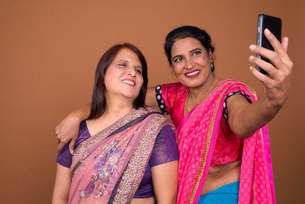 zwei reife indische Frauen, die traditionelle Sari-indische Kleidung zusammen mit Smartphone tragen