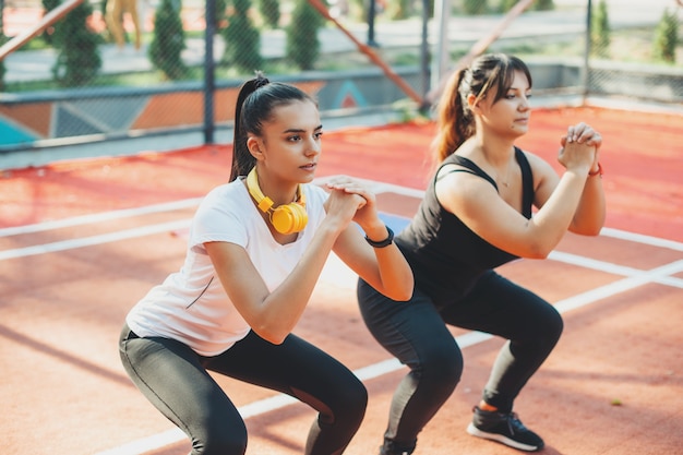 Zwei reizende junge Freundin, die Morgenstrecken in einem Sportpark macht, um fit zu werden. Junge Frau, die ihrer Freundin hilft, Gewicht zu verlieren.