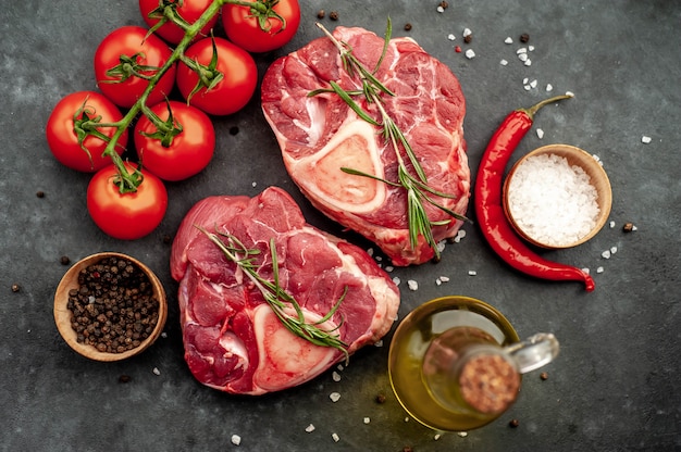 zwei rohe Rindfleischsteaks mit Knochen und Gewürzen auf einem Steinhintergrund