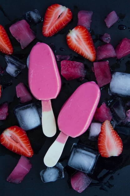 Zwei rosa Eiscreme auf einem schwarzen Hintergrund neben den geschnittenen Erdbeeren und dem gehackten Eis. Sommerkalte Wüste